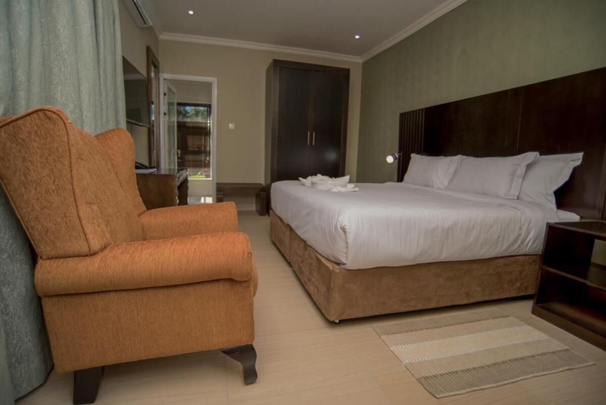 Een slaapkamer met een groot bed, een bruine fauteuil en een kledingkast.