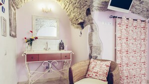 A bedroom with a stone arch, a bed with a patterned bedspread, a wicker chair, a vanity with a mirror, and a wall-mounted TV. - B&B Blu Bosa (Bosa)