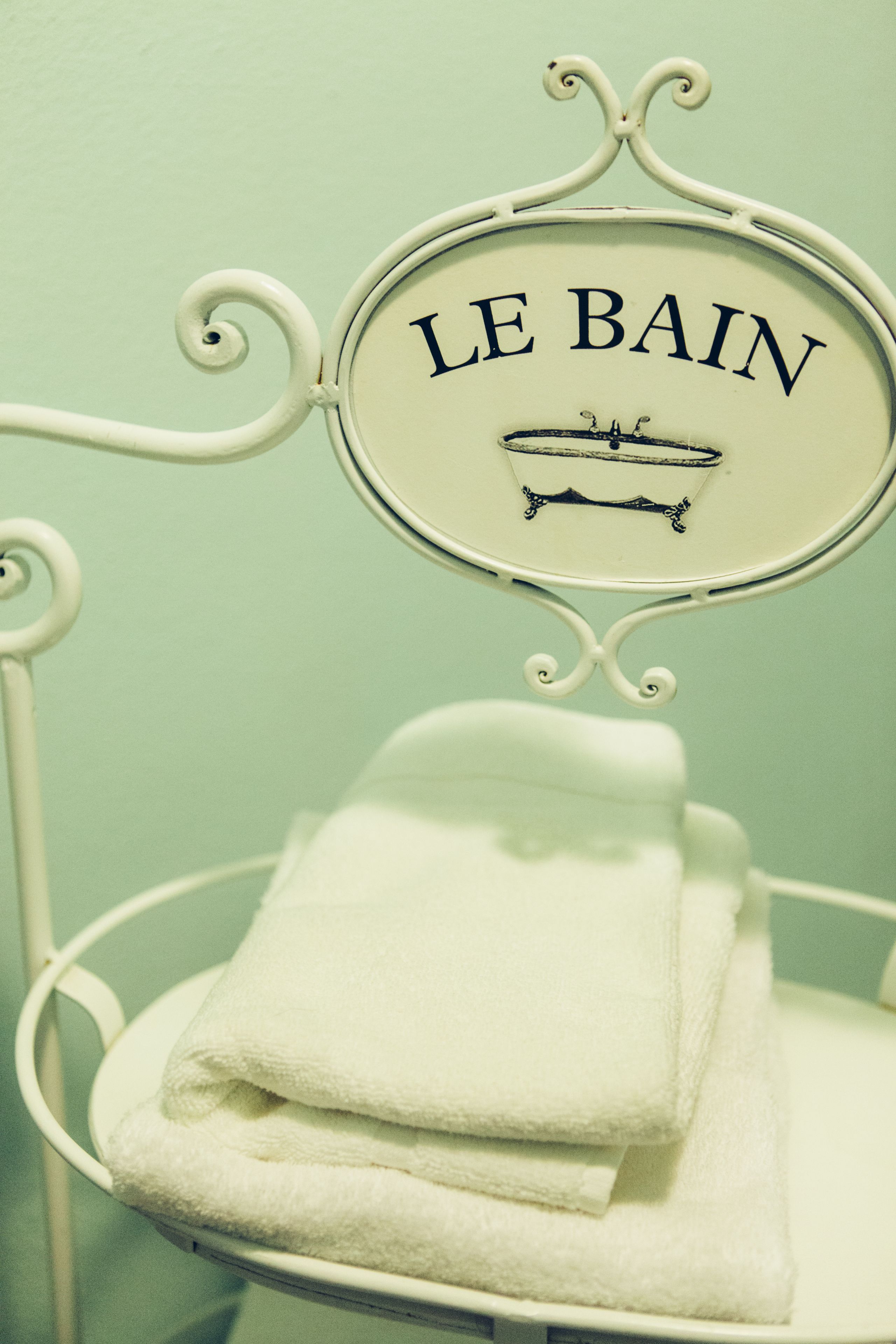 A sign with the text "LE BAIN" and a bathtub illustration, hanging above a stack of white towels.