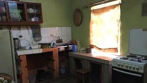 Cocina pequeña con electrodomésticos básicos, una ventana con cortinas y un taburete.