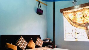 Un dormitorio con cama, almohadas, una mesita de noche, una ventana con cortina y un bolso colgado.