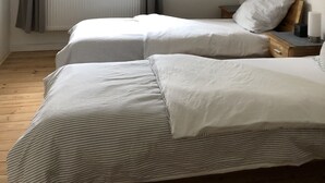 Un dormitorio con dos camas, una ventana con cortinas, un radiador, un cuadro enmarcado en la pared y una mesita de noche con una lámpara.