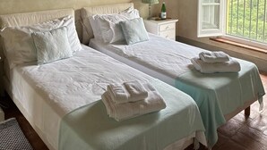 A bedroom with two beds, a large painting, a nightstand, a bottle, and a window with a view. - Luxury 6-bed Tuscan Villa Near Lucca and Florence (Capannori)