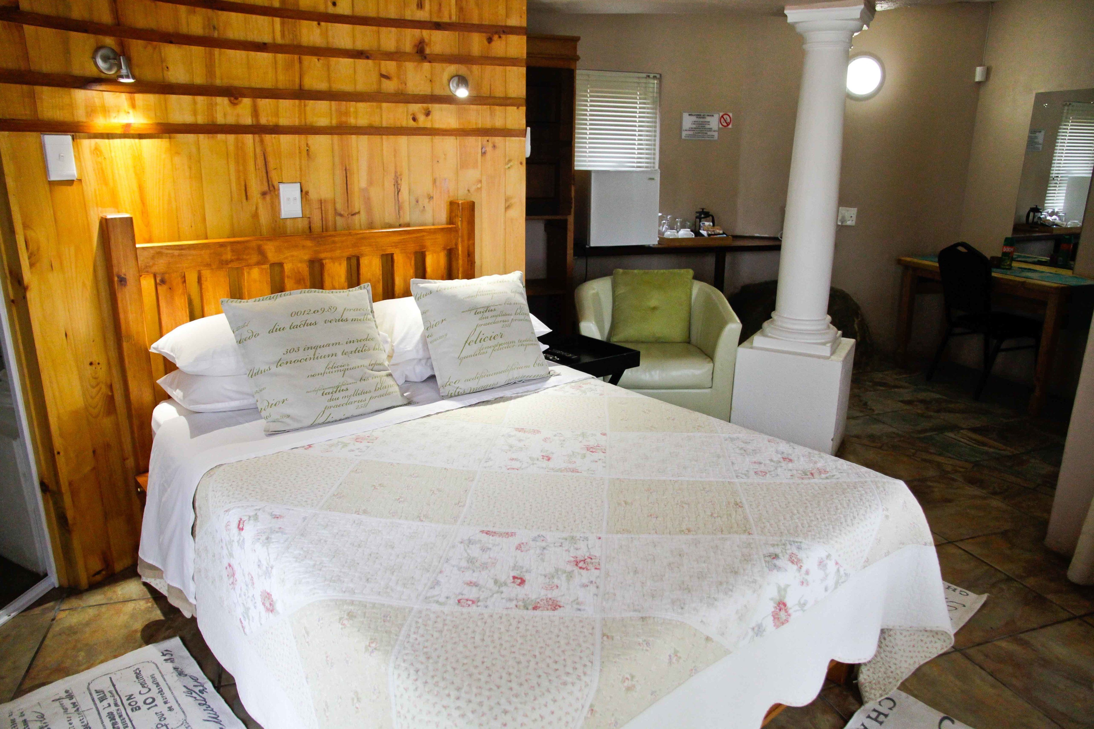 A bedroom with a wooden headboard, a bed with floral bedding, a green armchair, and a desk with a chair.