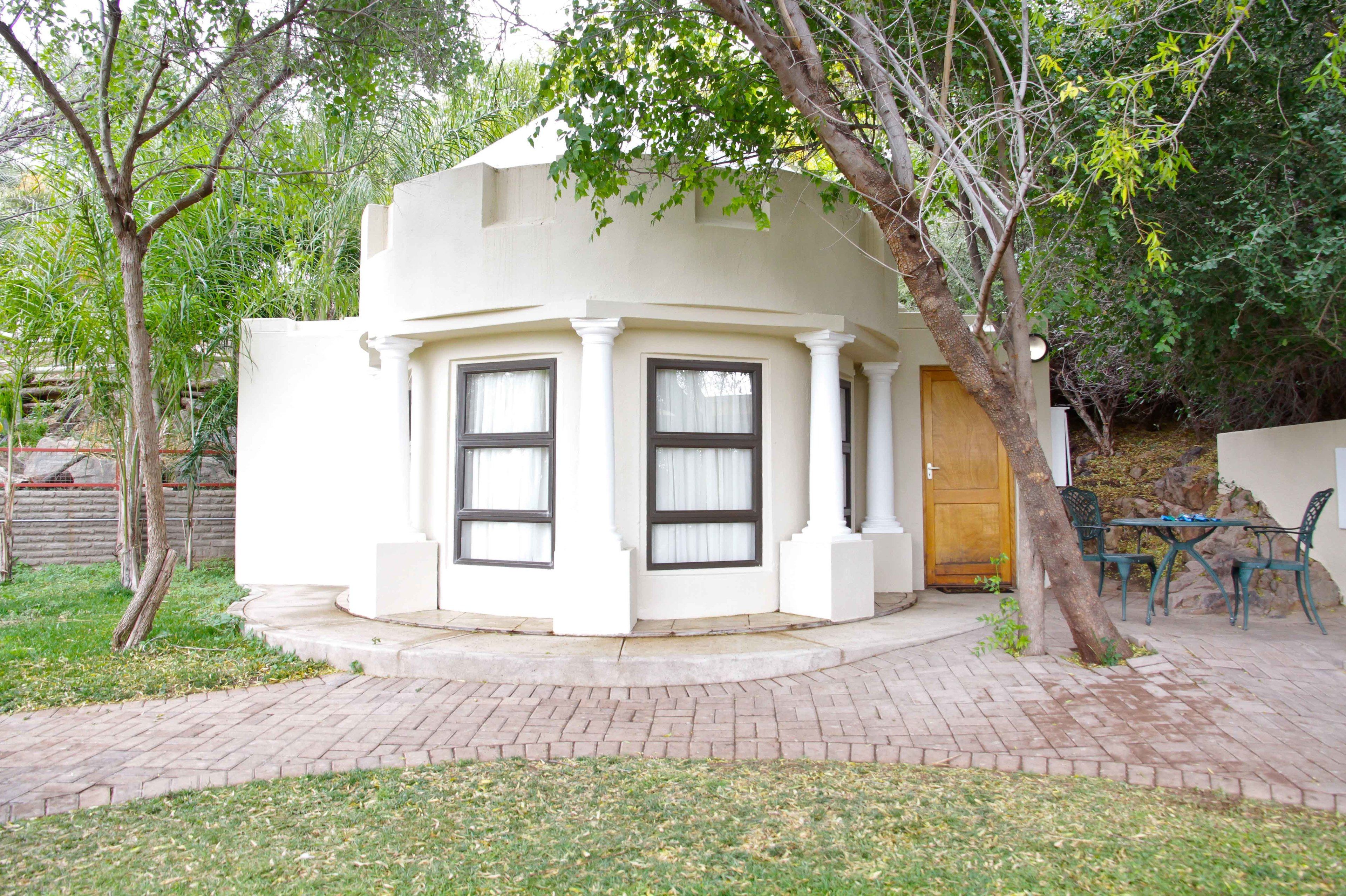 A corner building with a white exterior, two windows with dark frames, a wooden door, and a small outdoor seating area with a table and chairs.