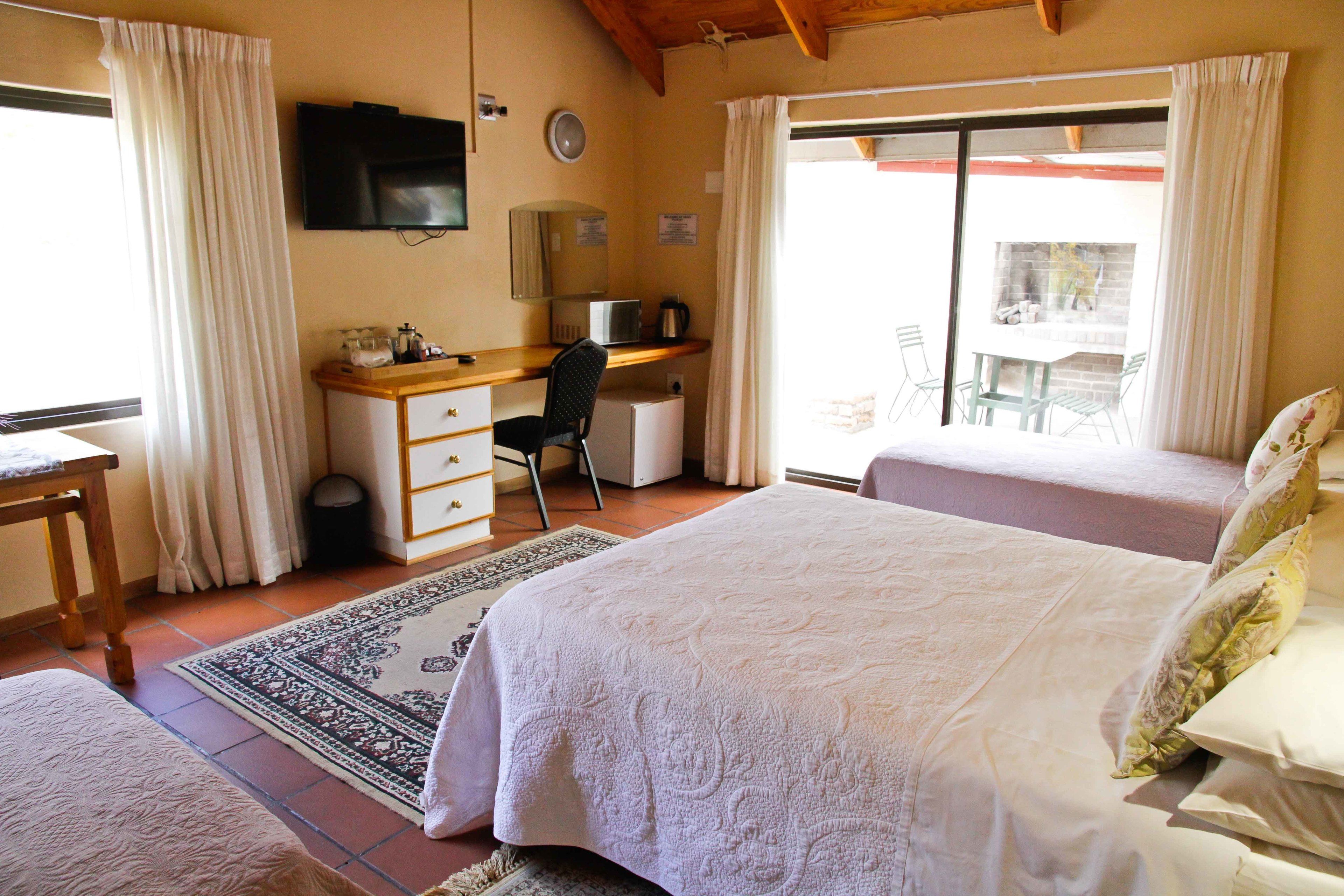 A bedroom with two beds, a desk, a chair, a TV, and a view of the outside.