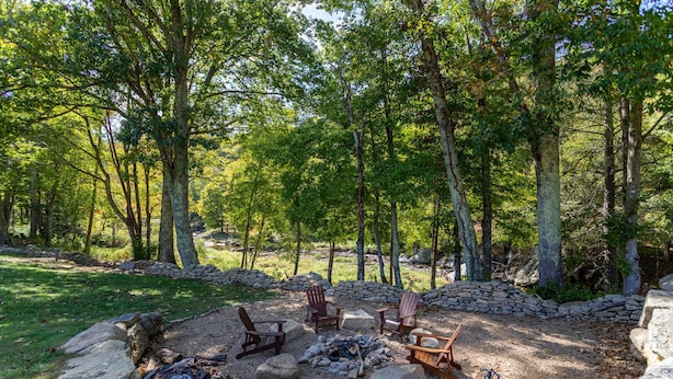 Campeggio immerso nella foresta, con un focolare, diverse sedie Adirondack e un muro in pietra.