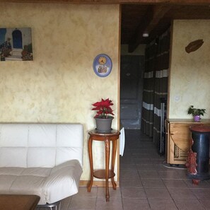 A room with a white sofa, a small wooden table with a potted plant, a wall clock, and a door leading to another room. - Quiet cottage with terrace, garden, pool in ST-VICTOR LA COSTE (GARD) (Saint-Victor-La-Coste)