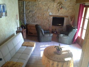 A living room with a stone wall, a white sofa, two leather armchairs, a coffee table, and a fireplace. - Quiet cottage with terrace, garden, pool in ST-VICTOR LA COSTE (GARD) (Saint-Victor-La-Coste)