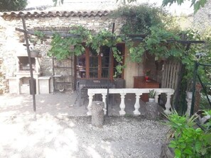 A stone building with a balcony, a wooden table, and a potted plant. - Quiet cottage with terrace, garden, pool in ST-VICTOR LA COSTE (GARD) (Saint-Victor-La-Coste)
