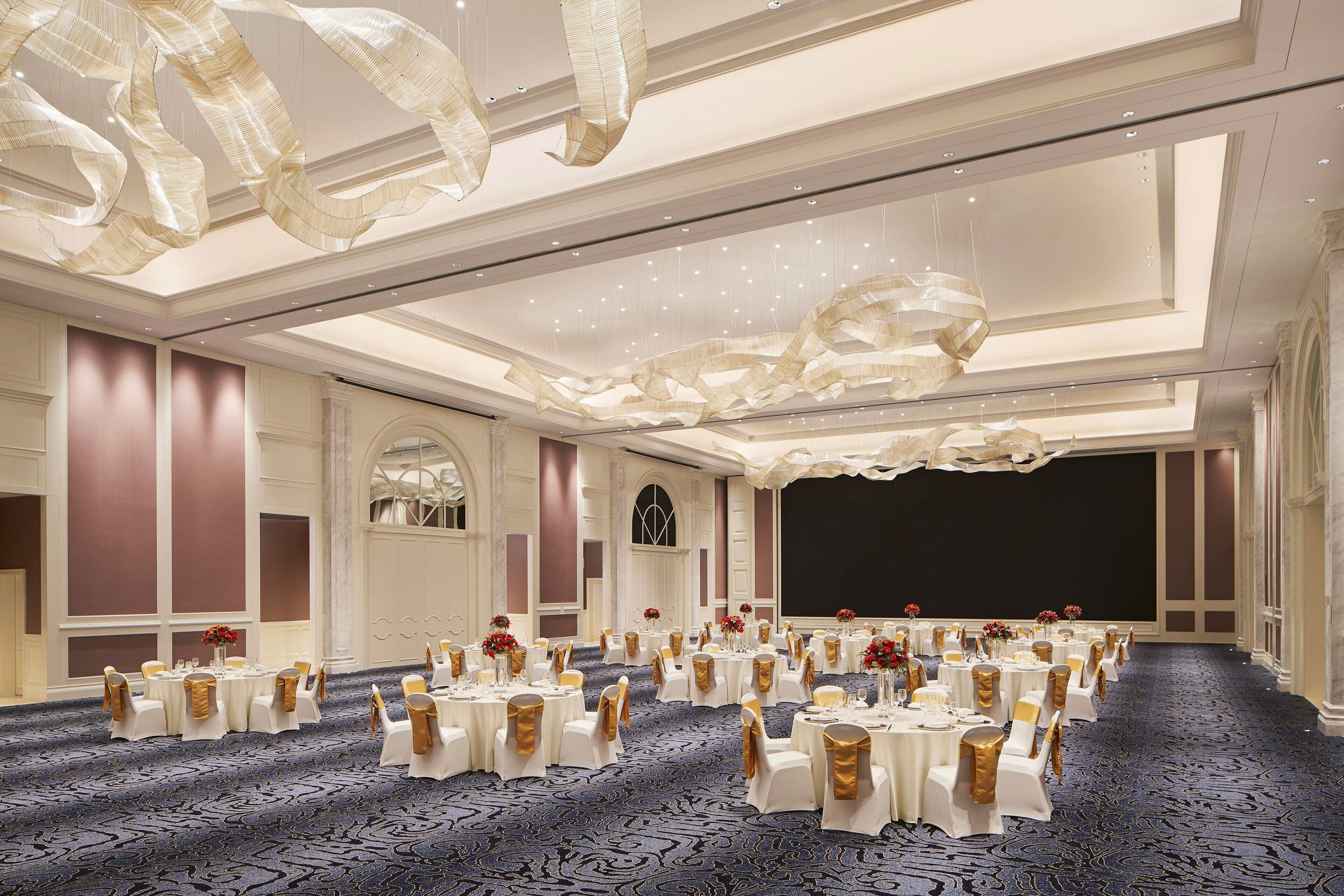 Un salón de banquetes con mesas redondas, manteles blancos y cintas doradas.