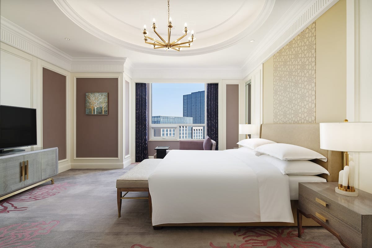 A spacious hotel room with a large bed, a television, a desk, and a view of the cityscape.