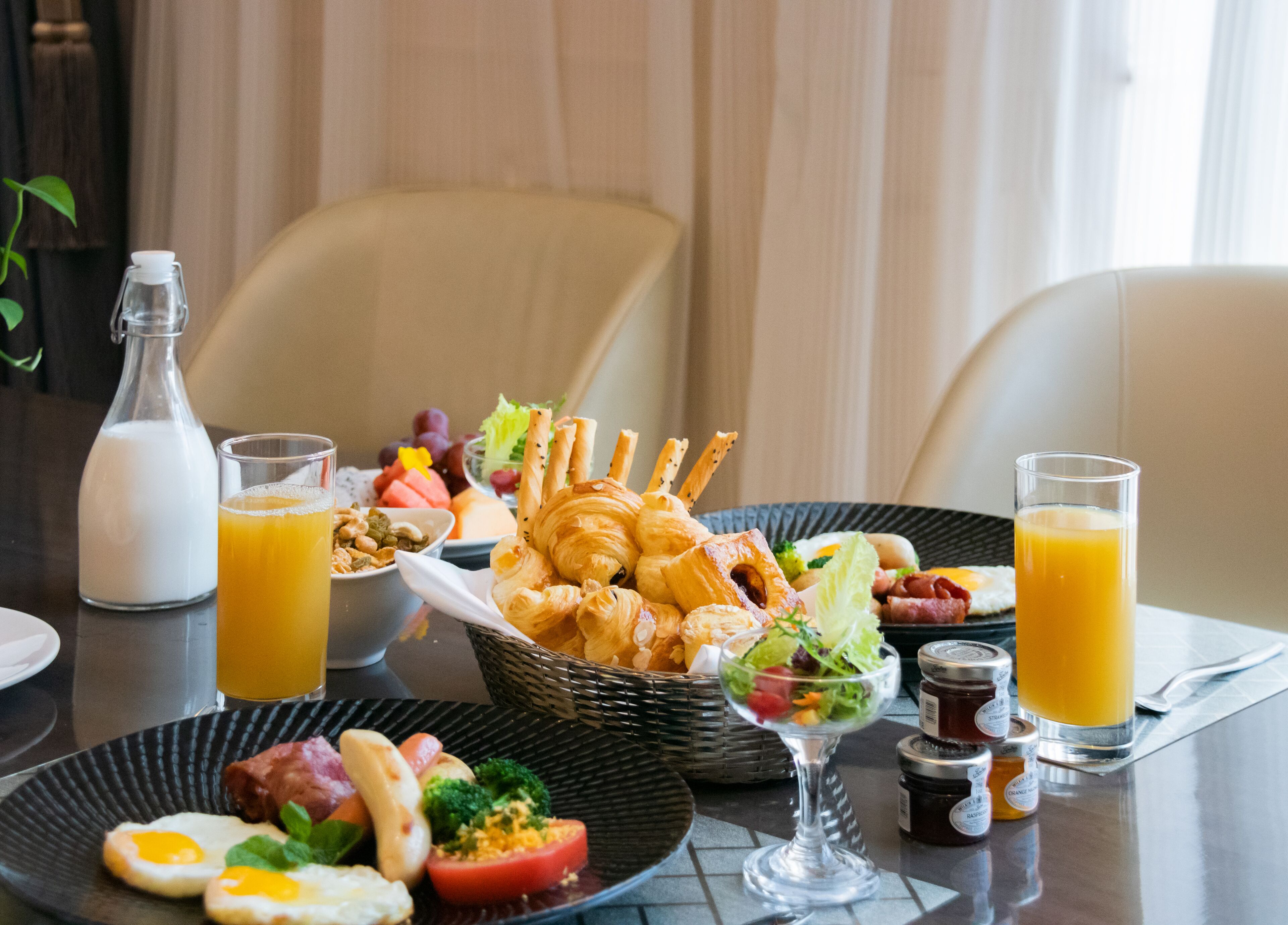A breakfast table with croissants, eggs, tomatoes, and juice.