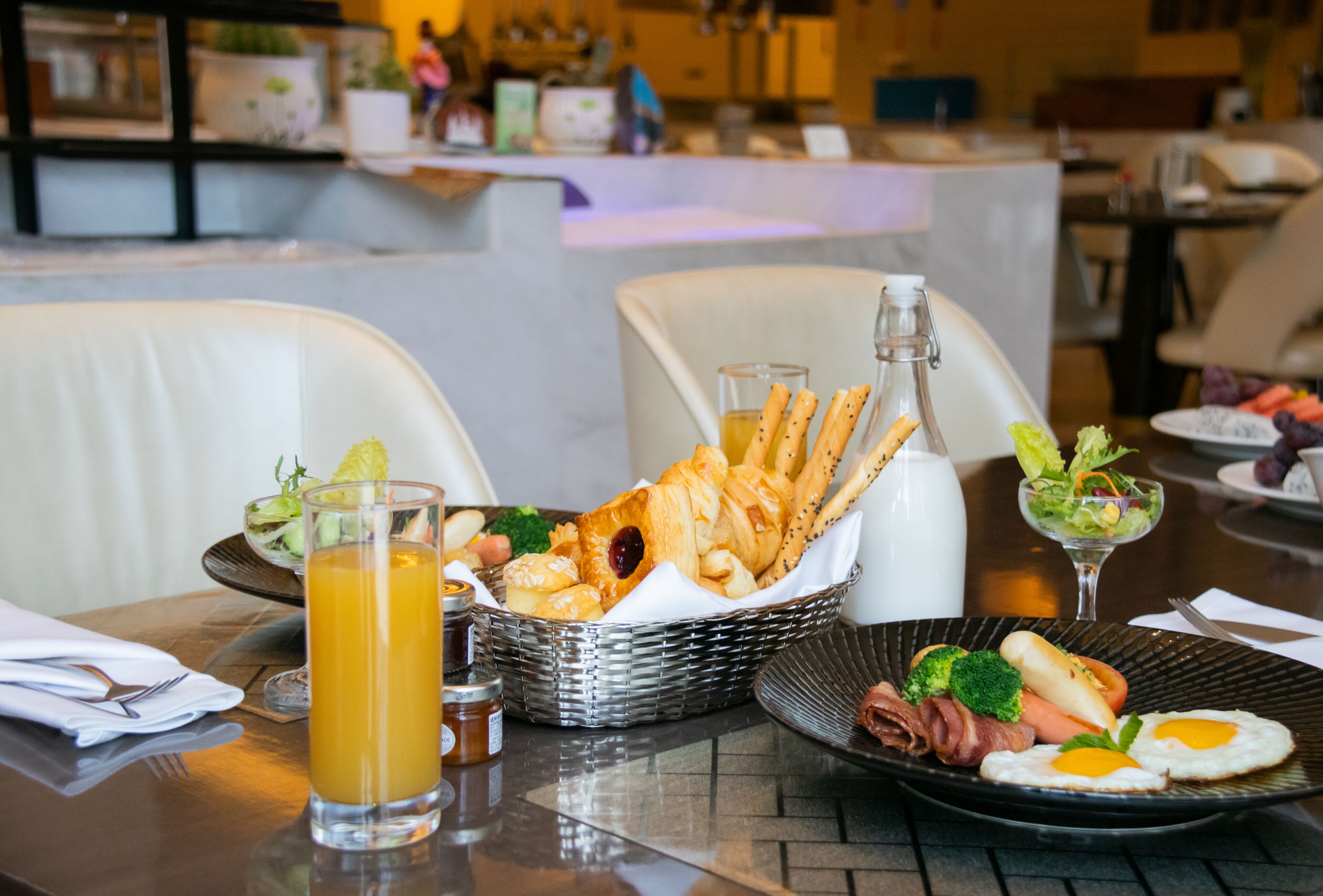 Ein Frühstückstisch mit Croissants, einer Milchflasche, einem Glas Orangensaft und einem Teller mit Eiern und Gemüse.