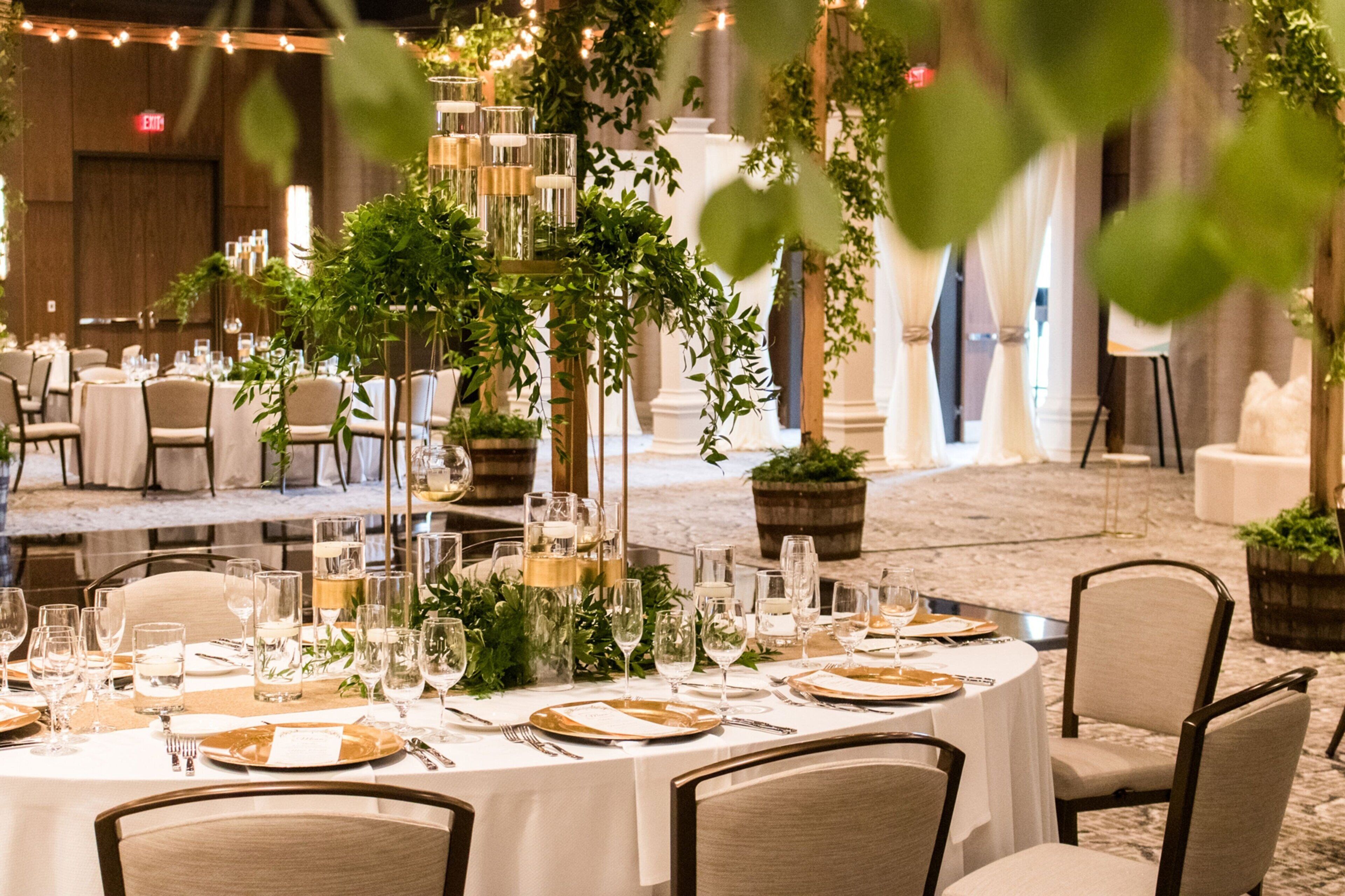 A banquet hall with round tables set for a formal event, featuring white tablecloths, gold cutlery, and glassware.
