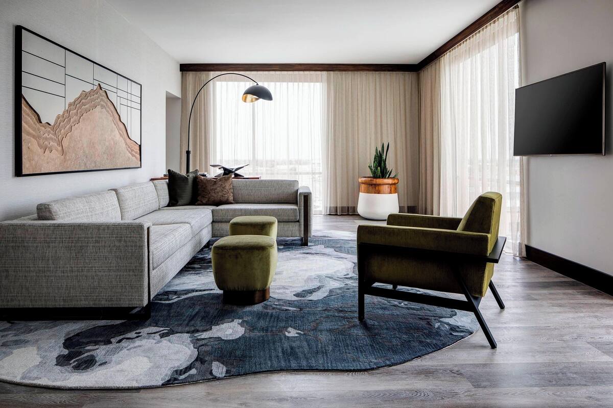 A modern living room with a sofa, ottomans, a chair, a floor lamp, a large painting, and a television.