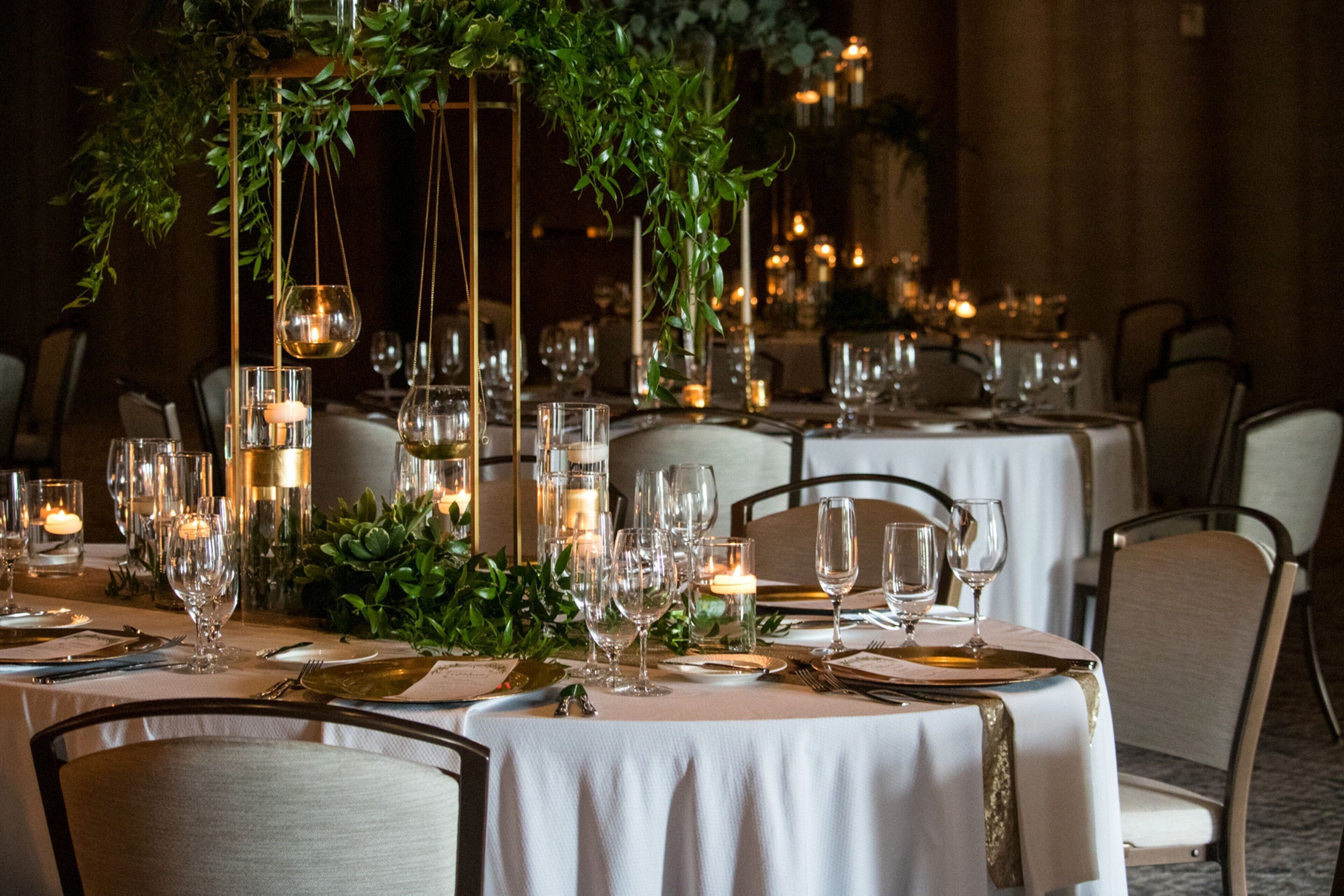 Un comedor con mesas dispuestas para una comida, con velas, copas y plantas.