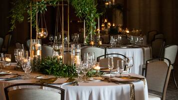 Un comedor con mesas dispuestas para una comida, con velas, copas y plantas.