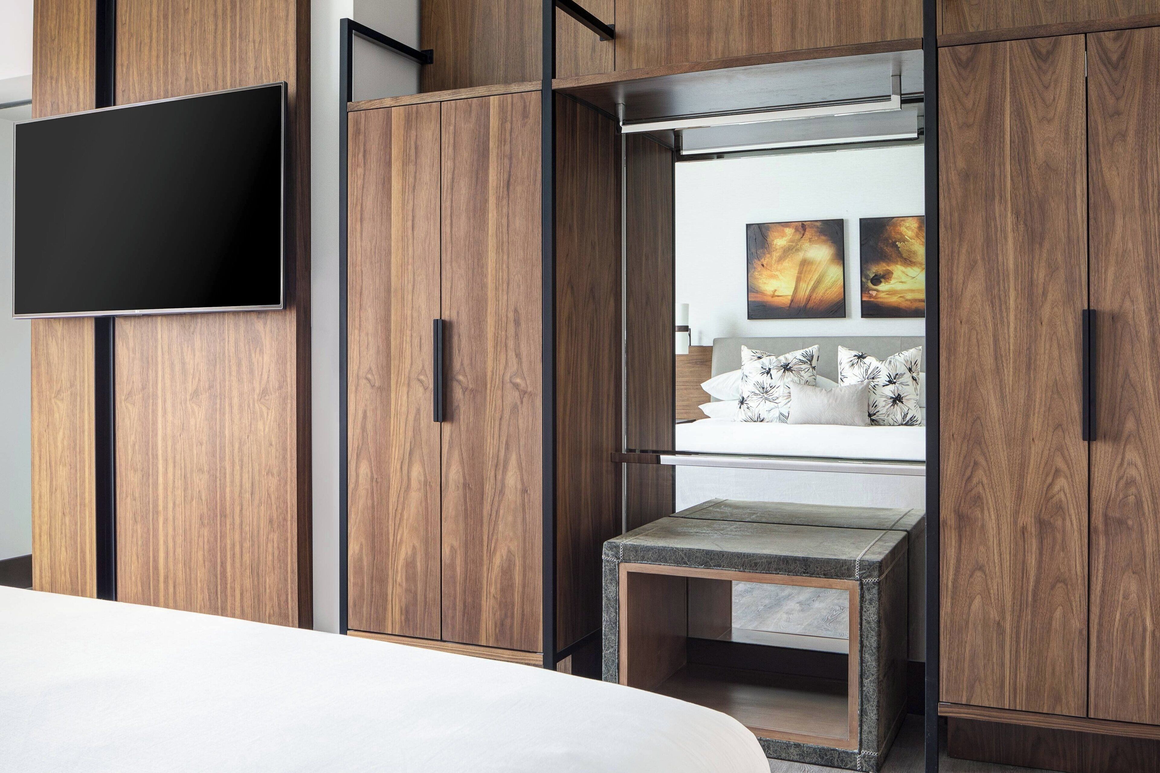 Un dormitorio moderno con una cama, un televisor montado en un mueble de madera y una pequeña mesa con un banco.