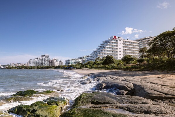 A beachfront hotel with multiple floors, a prominent red logo, and a view of the ocean.