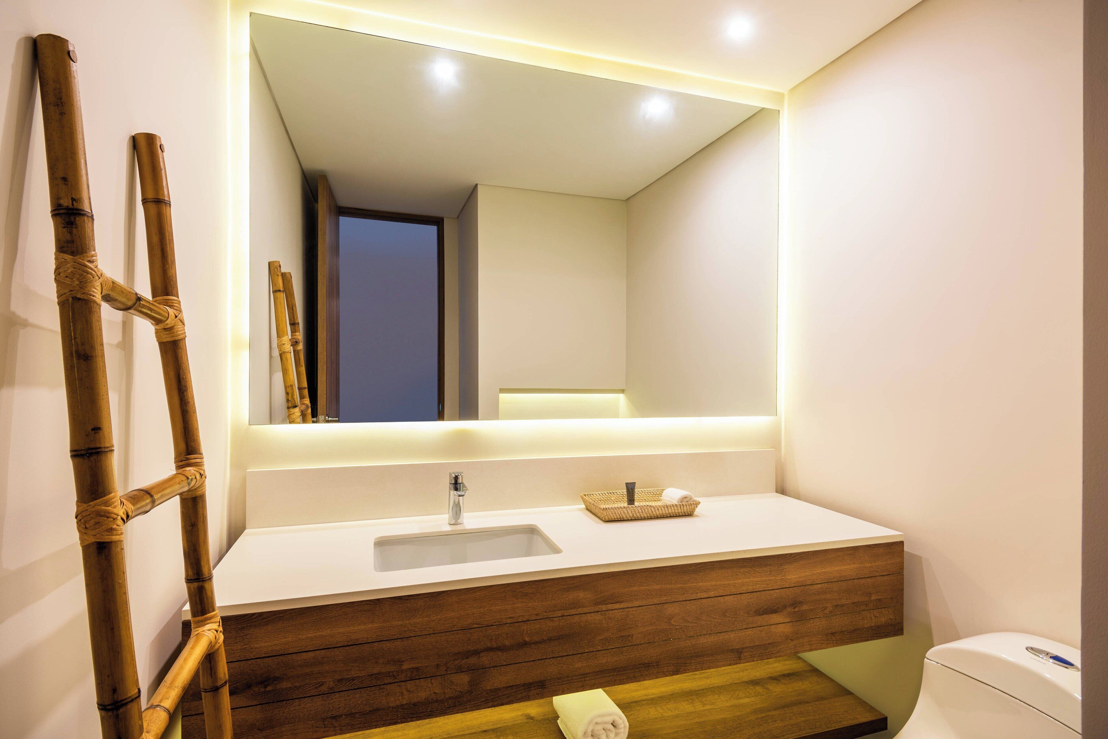 Un baño moderno con tocador de madera, un espejo grande y una escalera de bambú.