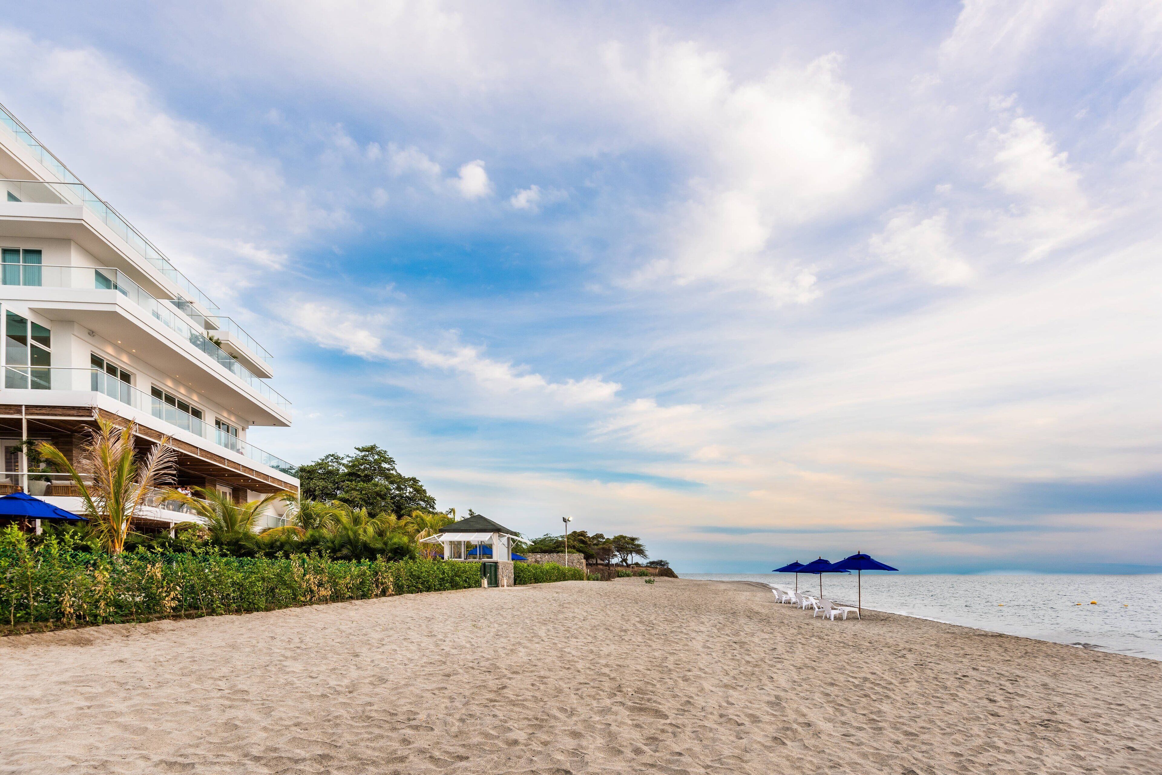 A beachfront hotel with a sandy beach, a pool area, and a view of the ocean.