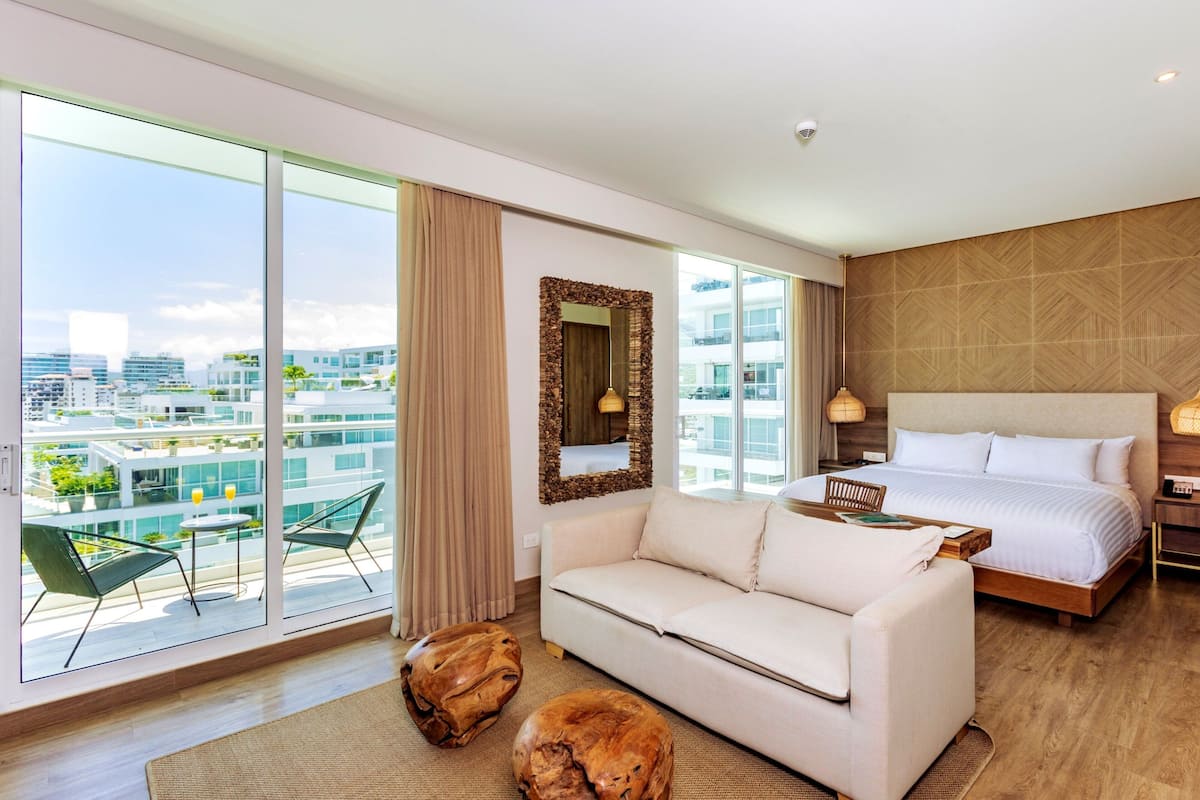 Een moderne hotelkamer met een groot balkon, een bank, een bed en een houten bijzettafeltje.