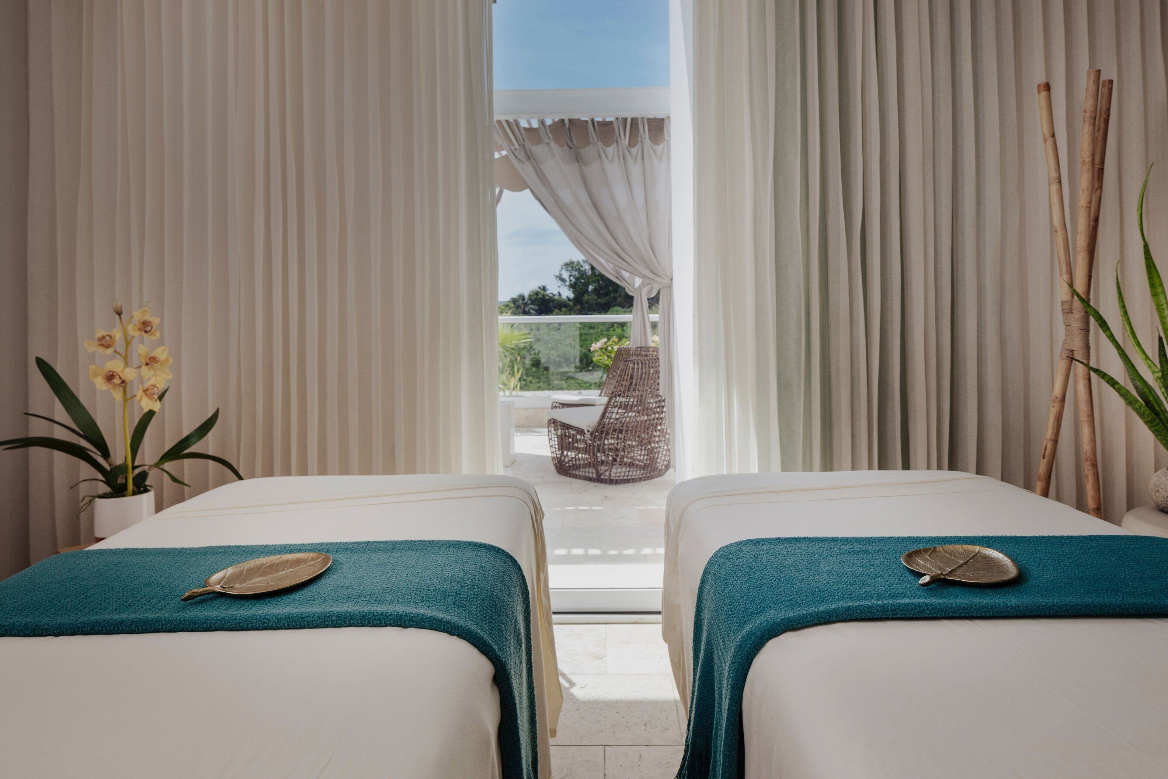 A room with two beds, a potted plant, and a view of an outdoor seating area.
