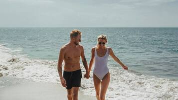 Two people walking on a beach with the ocean in the background.