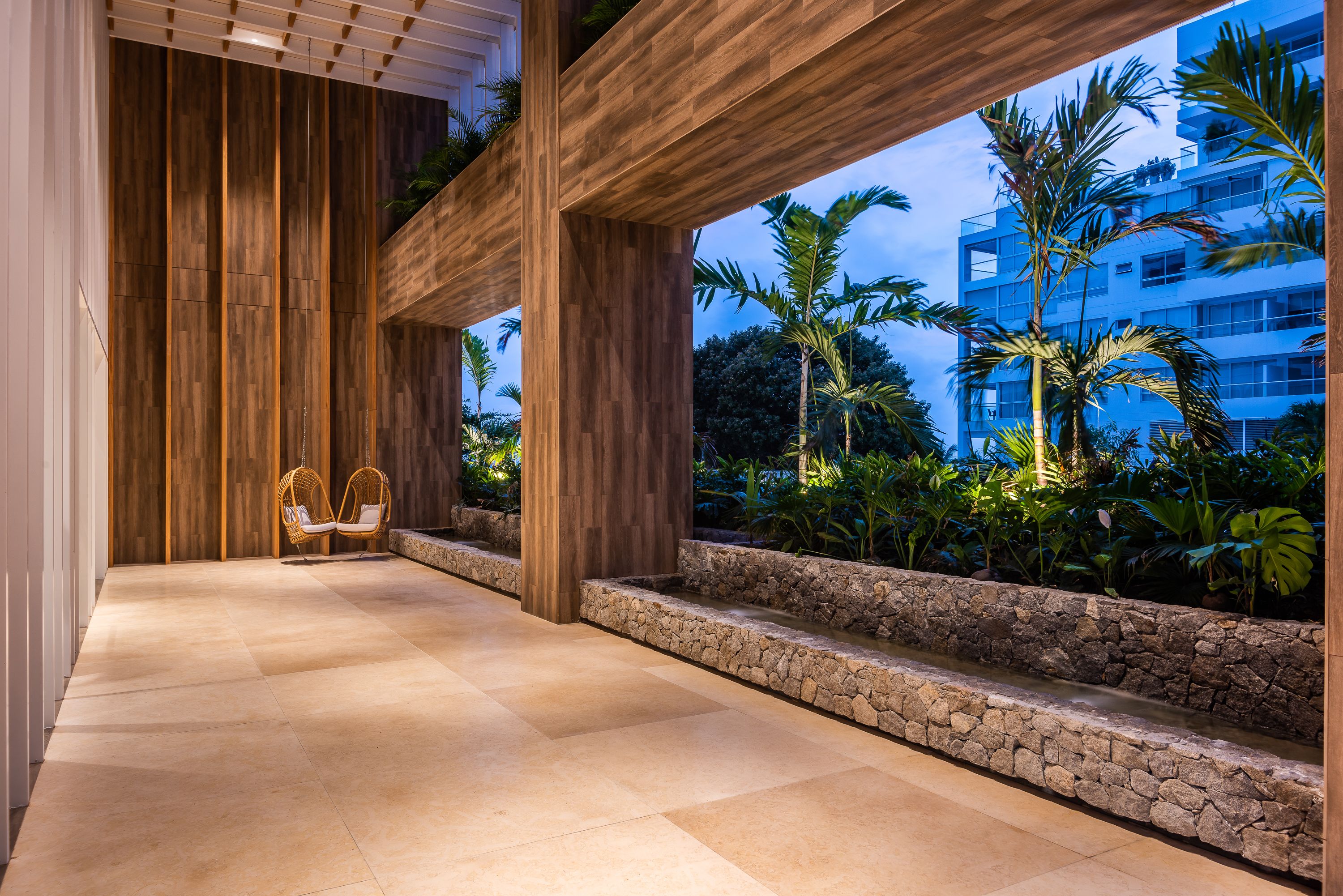 A spacious indoor area with a wooden floor, a stone bench, and a wicker chair.