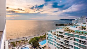 A high-rise hotel with a pool, a beach view, and a sunset over the ocean.