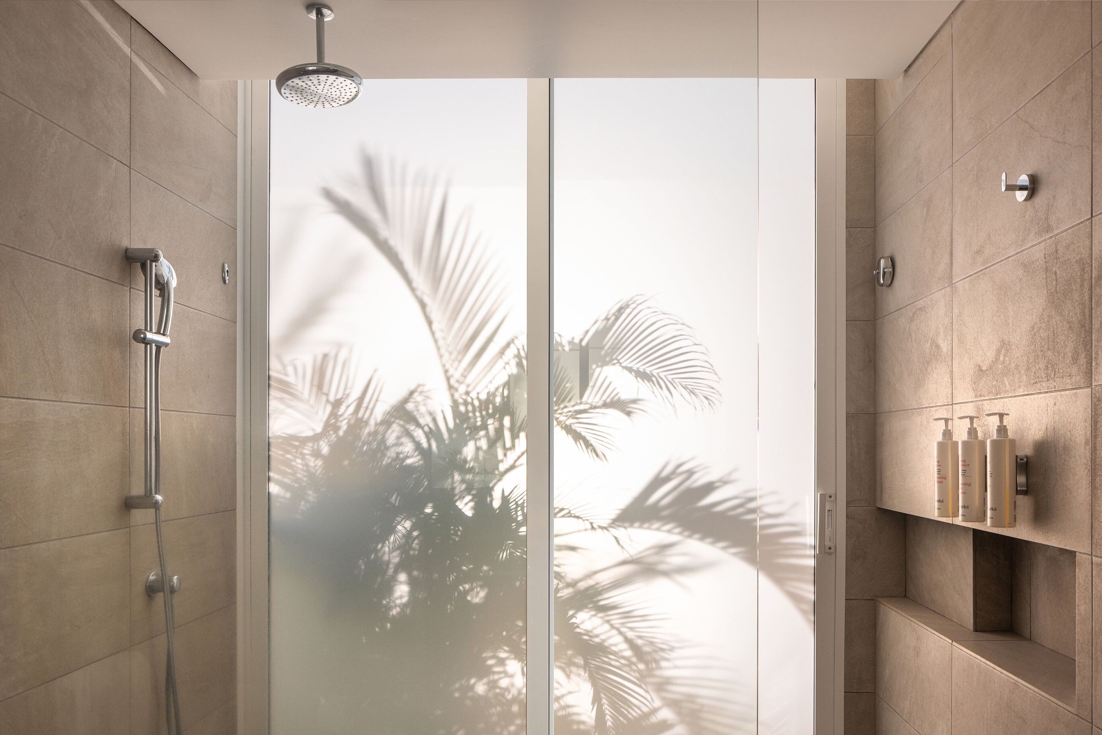 A modern bathroom with a glass door, a shower, and a shelf with toiletries.