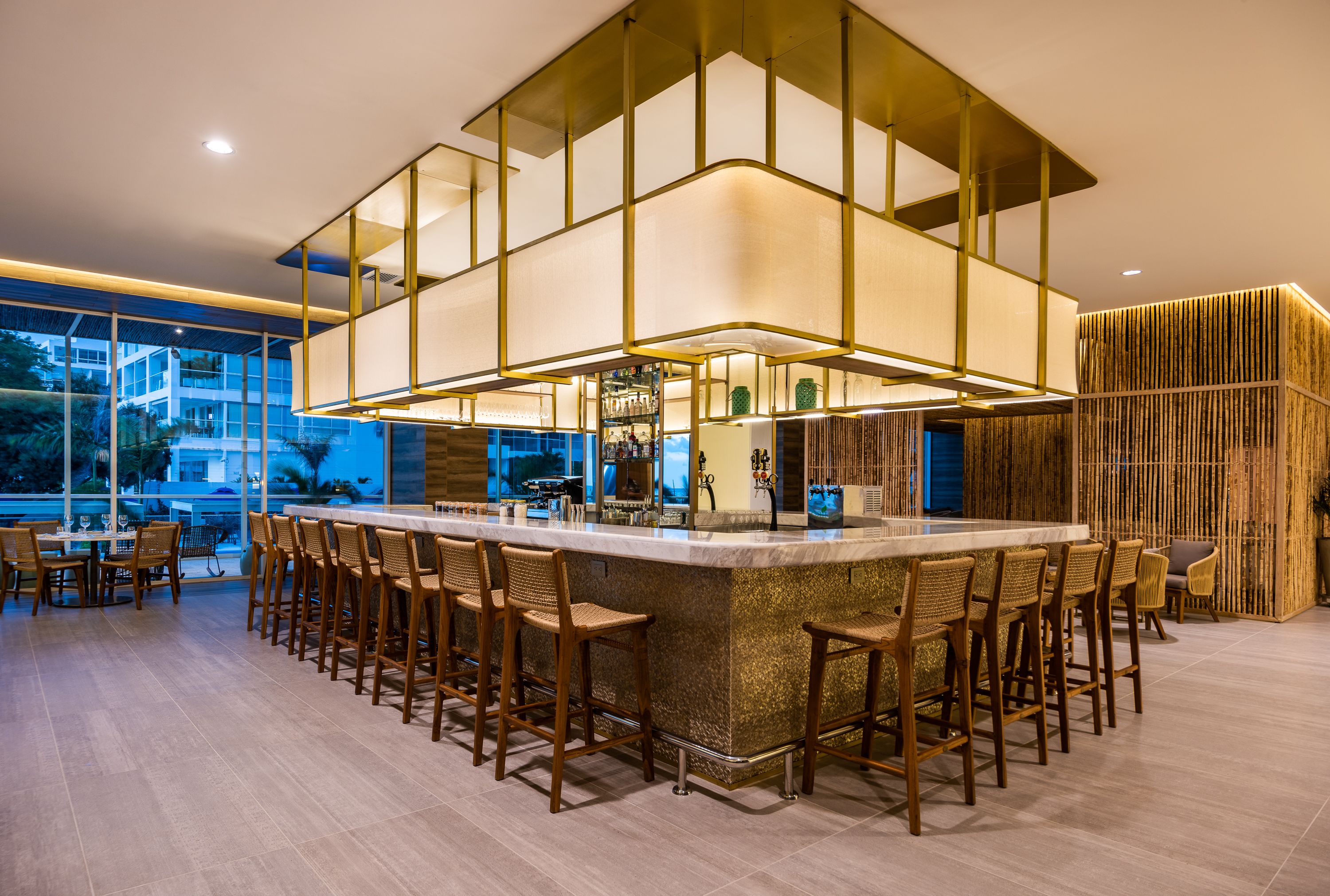 A modern bar area with a central island, bar stools, and a high ceiling with geometric lighting.