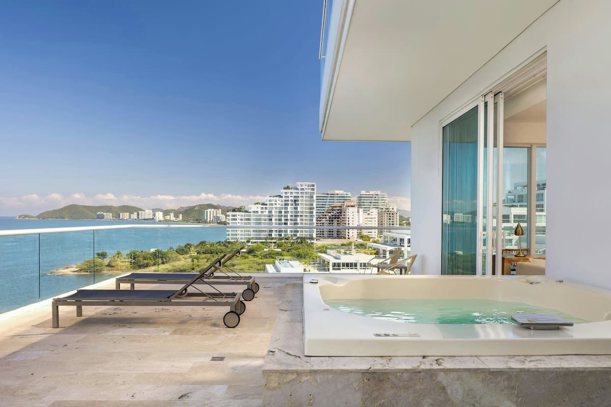 Een balkon met een jacuzzi, lounge stoelen en uitzicht op zee en gebouwen.