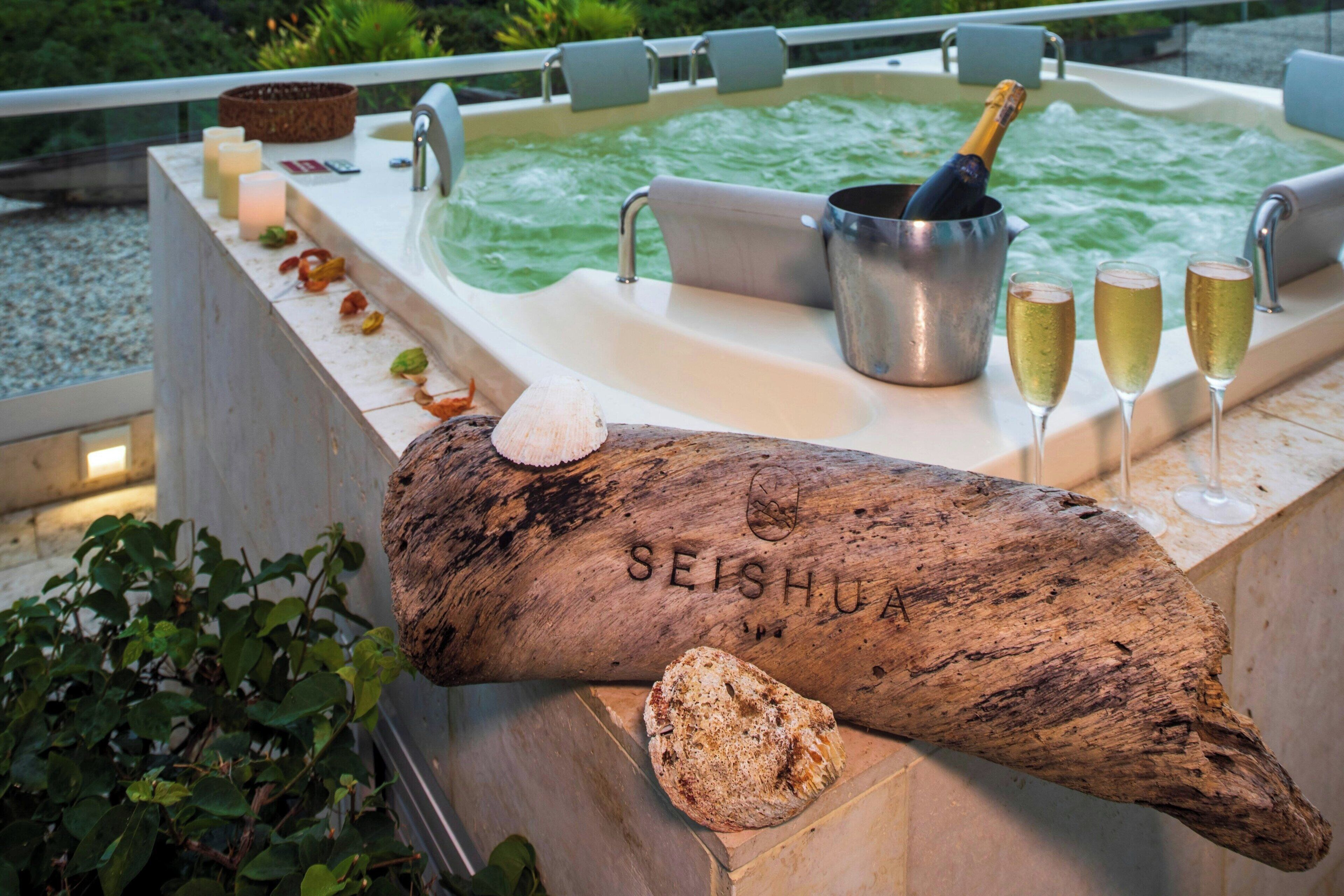 A hot tub with a wooden log, candles, and champagne glasses.