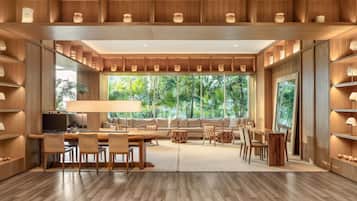Relax in a spacious living area with a high ceiling, featuring a large window offering a view of lush greenery and a comfortable seating area with a sofa and chairs.