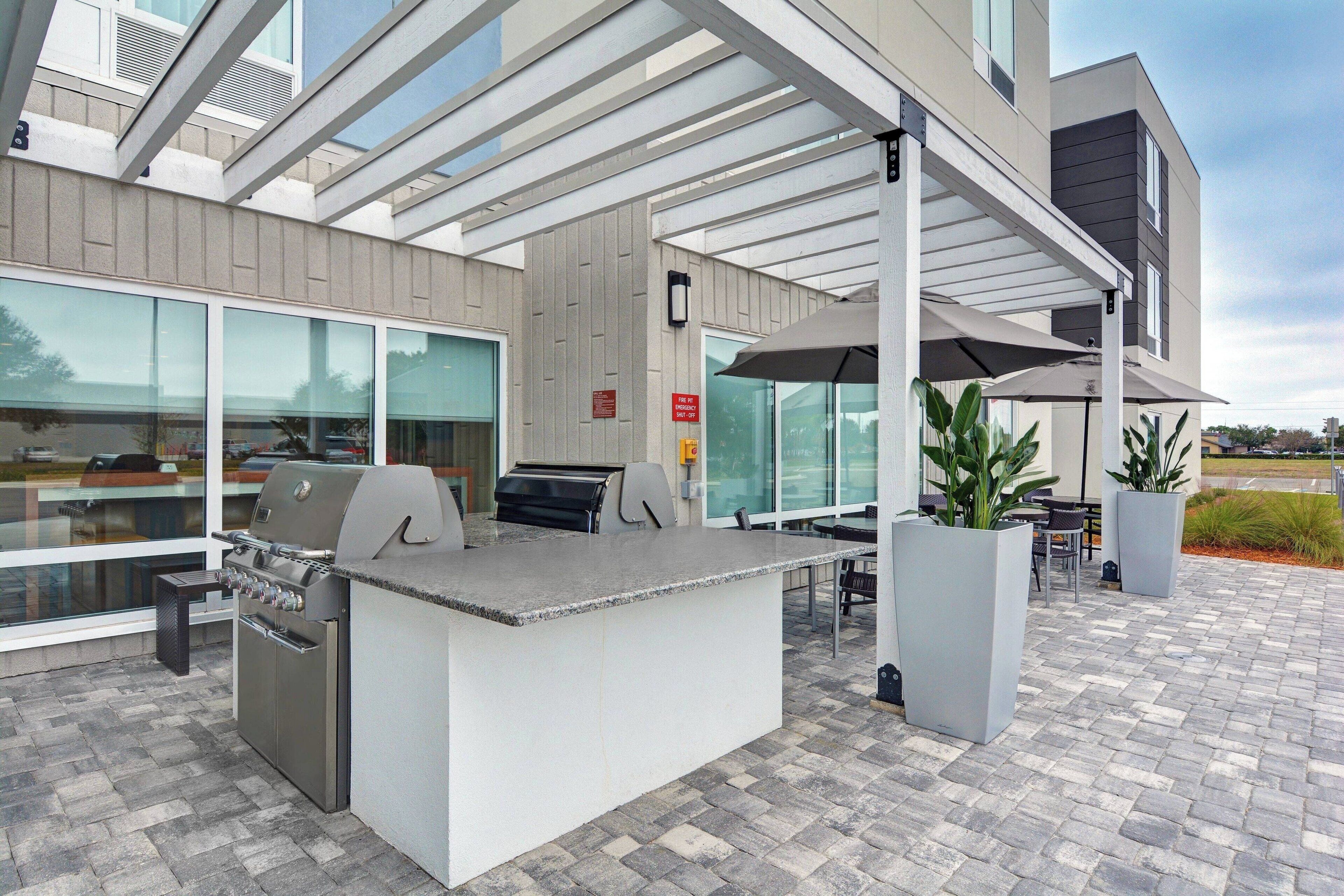 An outdoor patio area with a barbecue station, seating, and potted plants.