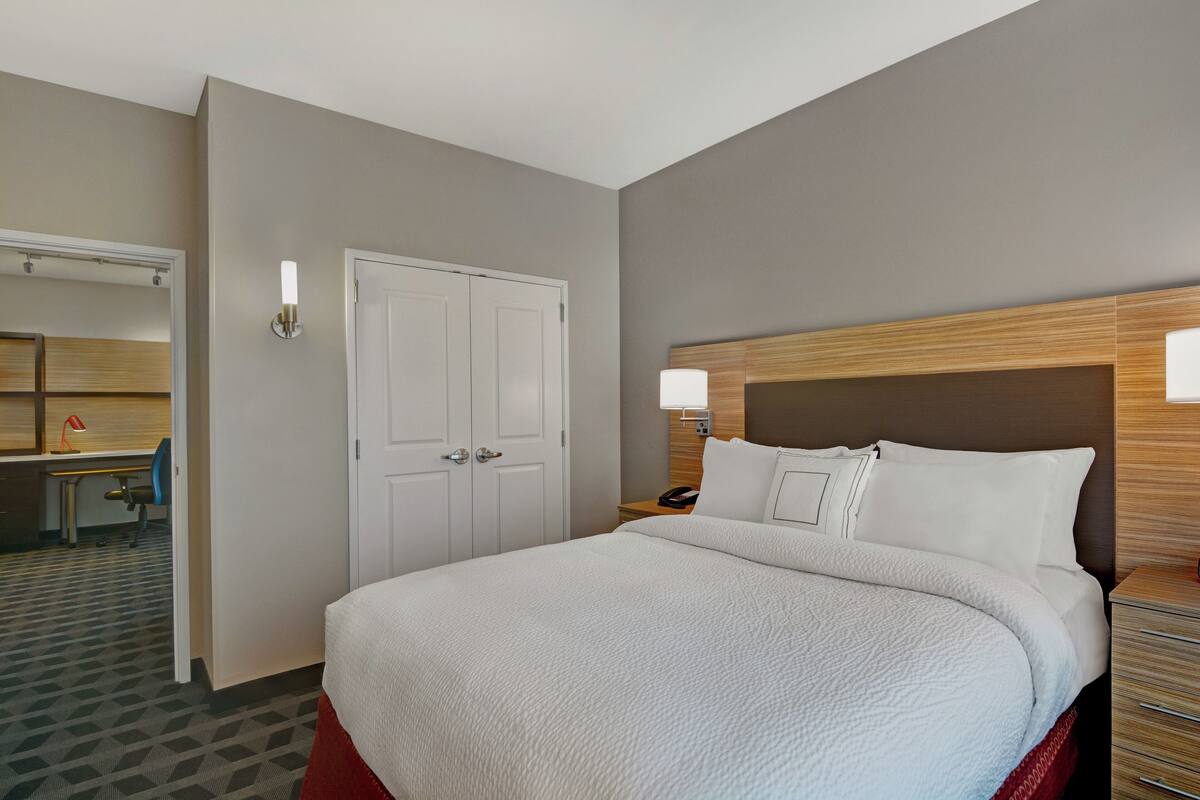 Quarto de hotel com uma cama grande, uma escrivaninha com cadeira, um guarda-roupa e um espelho.