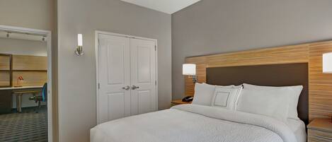 A hotel room with a large bed, a desk with a chair, a wardrobe, and a mirror.