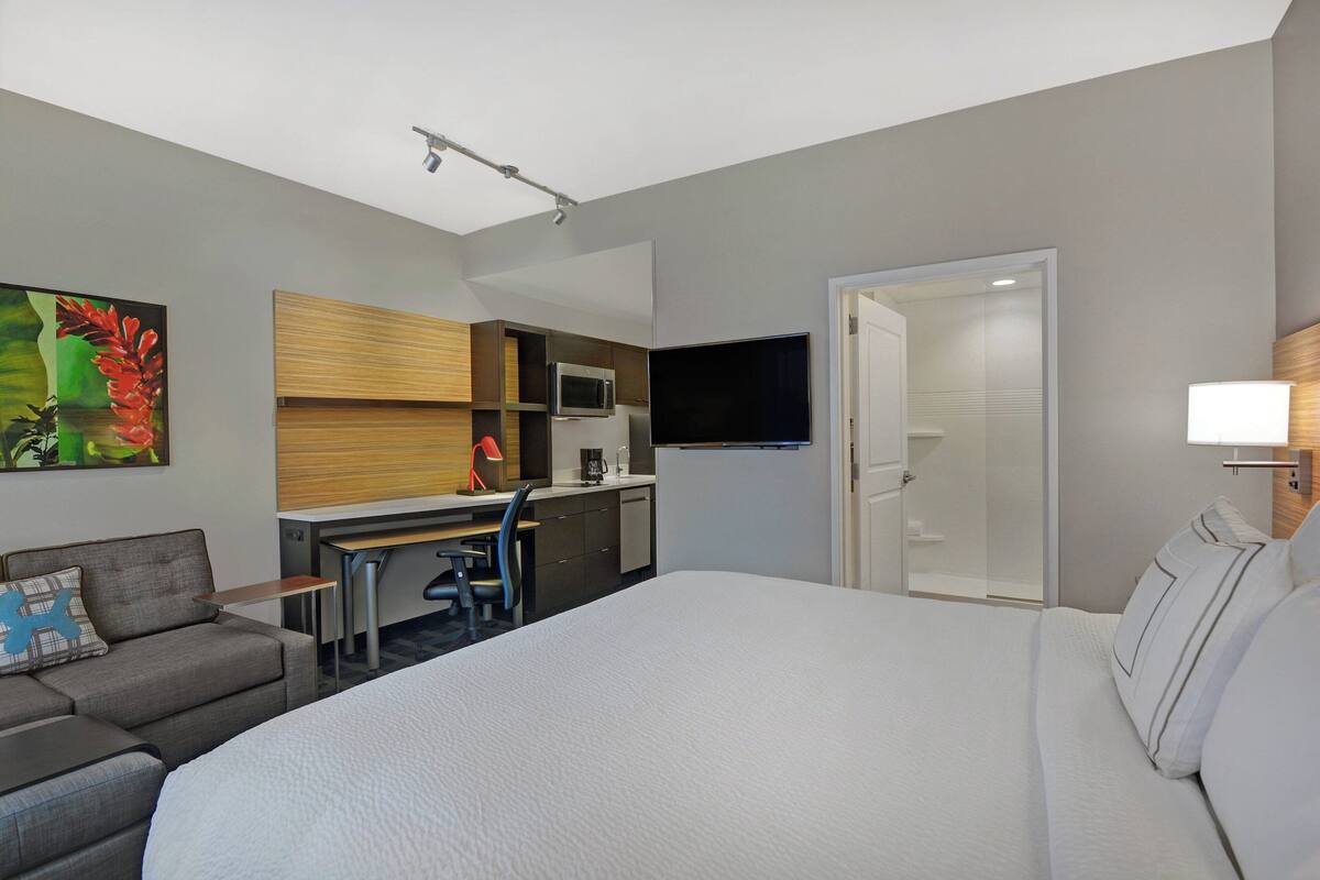 Quarto de hotel com cama grande, sofá, escrivaninha com computador, micro-ondas e televisão.