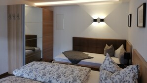A modern bedroom with a wooden headboard, a bed with floral bedding, a bedside table with a lamp, and a wardrobe with a mirror.