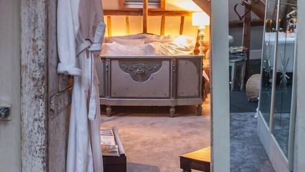 Een slaapkamer met een schuine kap, een bed, een nachtkastje en een raam.