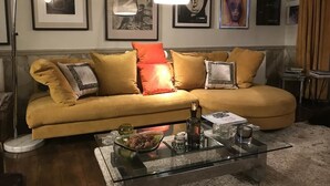 Een woonkamer met een gele bank, een glazen salontafel en lijstwerken aan de muur.