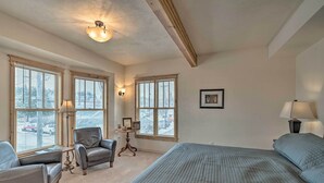 A bedroom with a large bed, two armchairs, a small table, and a window with blinds. - Updated Townhome w/ Hot Tub - Walk to Downtown! (Red Lodge)
