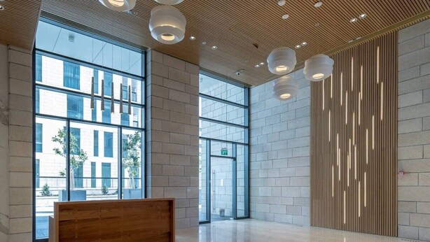 A spacious lobby with large windows, a wooden reception desk, and modern pendant lighting. - Beautiful 1 bedroom in great central area (Jerusalem)