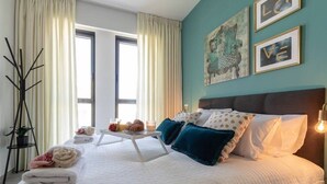 A neatly made bed with pillows, a bedside table with a lamp, and a window with curtains. - Beautiful 1 bedroom in great central area (Jerusalem)