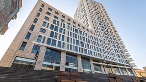 A modern high-rise building with a prominent glass facade, multiple balconies, and a series of steps leading to the entrance. - Beautiful 1 bedroom in great central area (Jerusalem)