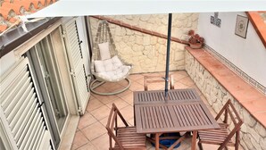 Une petite terrasse extérieure avec une table et des chaises, un fauteuil suspendu et un mur en pierre.