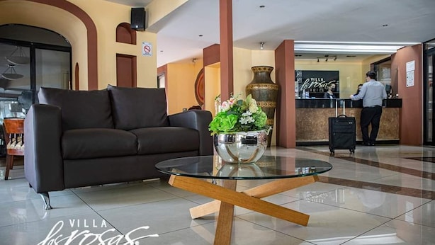 A lobby with a black sofa, a glass coffee table, and a reception desk. - Hotel Villa las Rosas (Tepic)