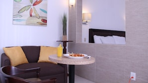 A modern room with a sofa, a small round table with a plate of food and a drink, a lamp, and a painting on the wall. - Hotel Villa las Rosas (Tepic)